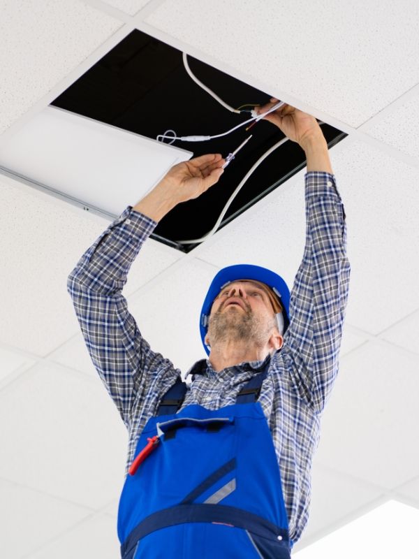Electrician installing emergency lighting in commercial ceiling.