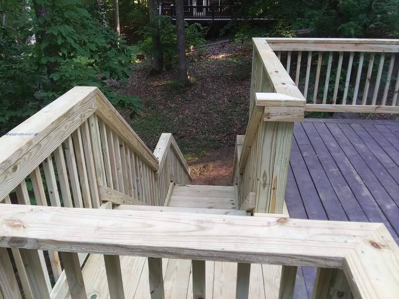 Wooden deck with stairs leading down into a wooded area. Light brown railing and steps.