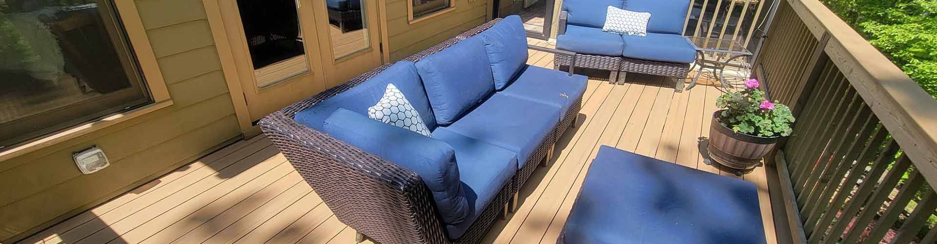 Outdoor deck with blue couches, wooden railing, and potted flowers.