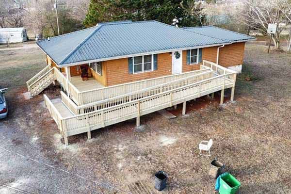 Brick house with ramp access and metal roof. Wooden deck extends from the entrance.