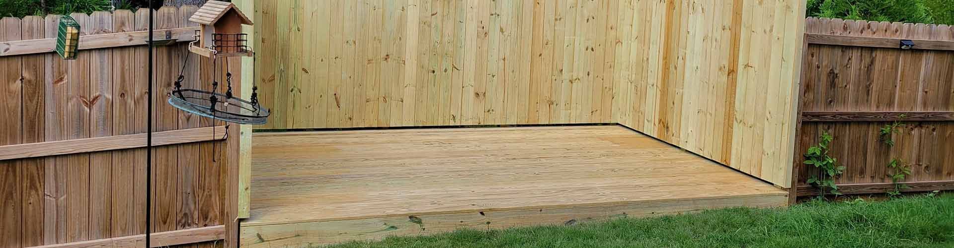 Wooden fences enclose a grass yard with a wooden structure. A bird feeder stands near one fence.