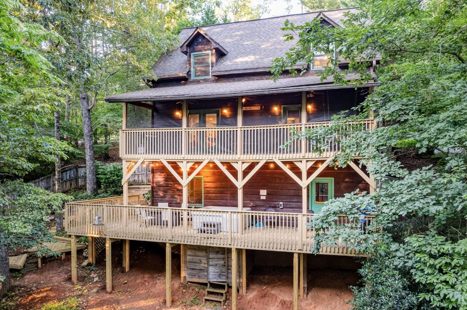 Wooden cabin with decks, surrounded by trees, with a turquoise door.