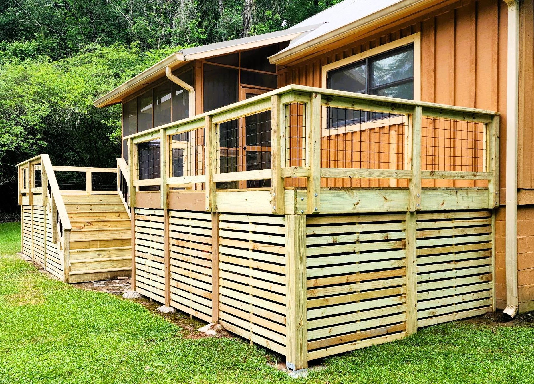 Wooden deck with stairs, built against a brown house. Green grass surrounds it.