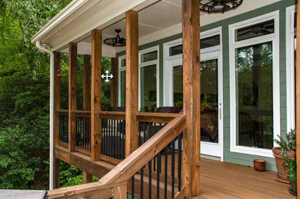 Wooden deck with railing and supporting columns. Green siding with white-framed glass doors and windows.
