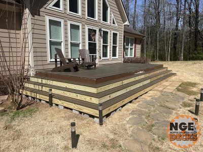 Composite deck with steps, two chairs, and landscape lights in front of a house.