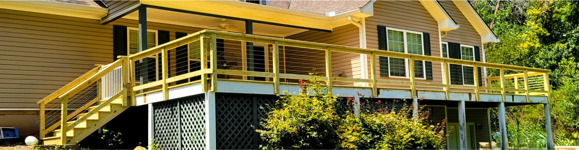 Wooden house with a porch and steps, surrounded by green trees.