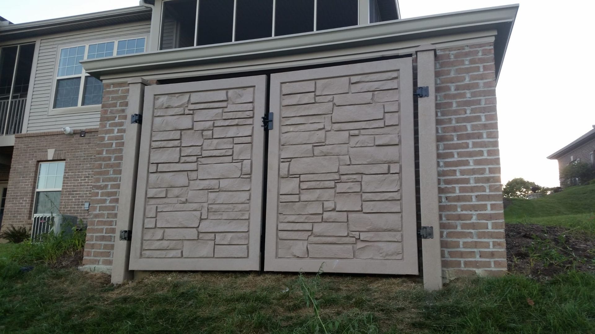 A concrete fence surrounds a brick driveway with a house in the background. A concrete fence surrounds a brick driveway with a house in the background.