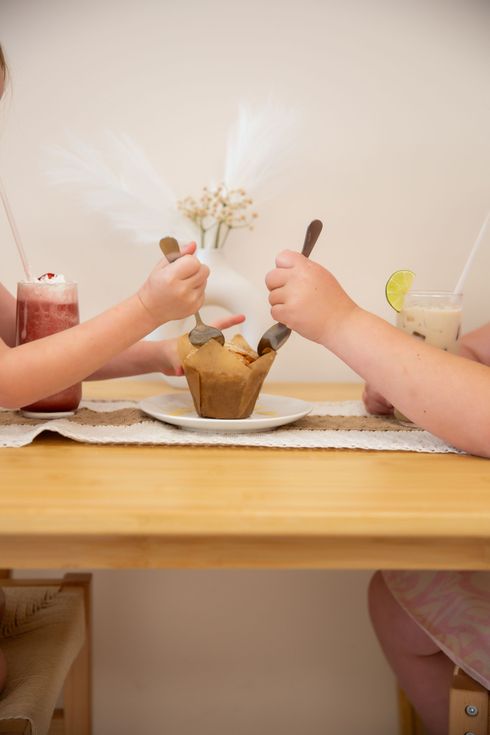 Homemade muffin being shared by two little girls for breakfast with drinks at covenant cafe.
