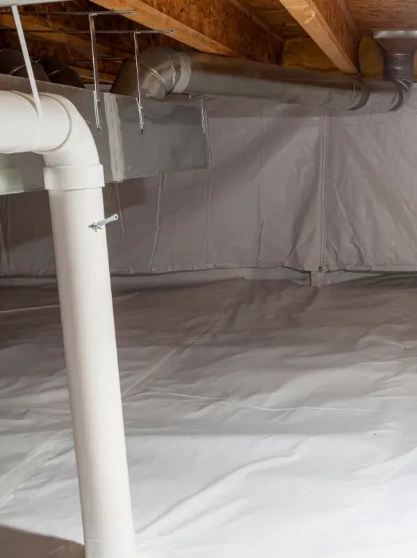A basement with a lot of pipes and a white tarp on the floor.