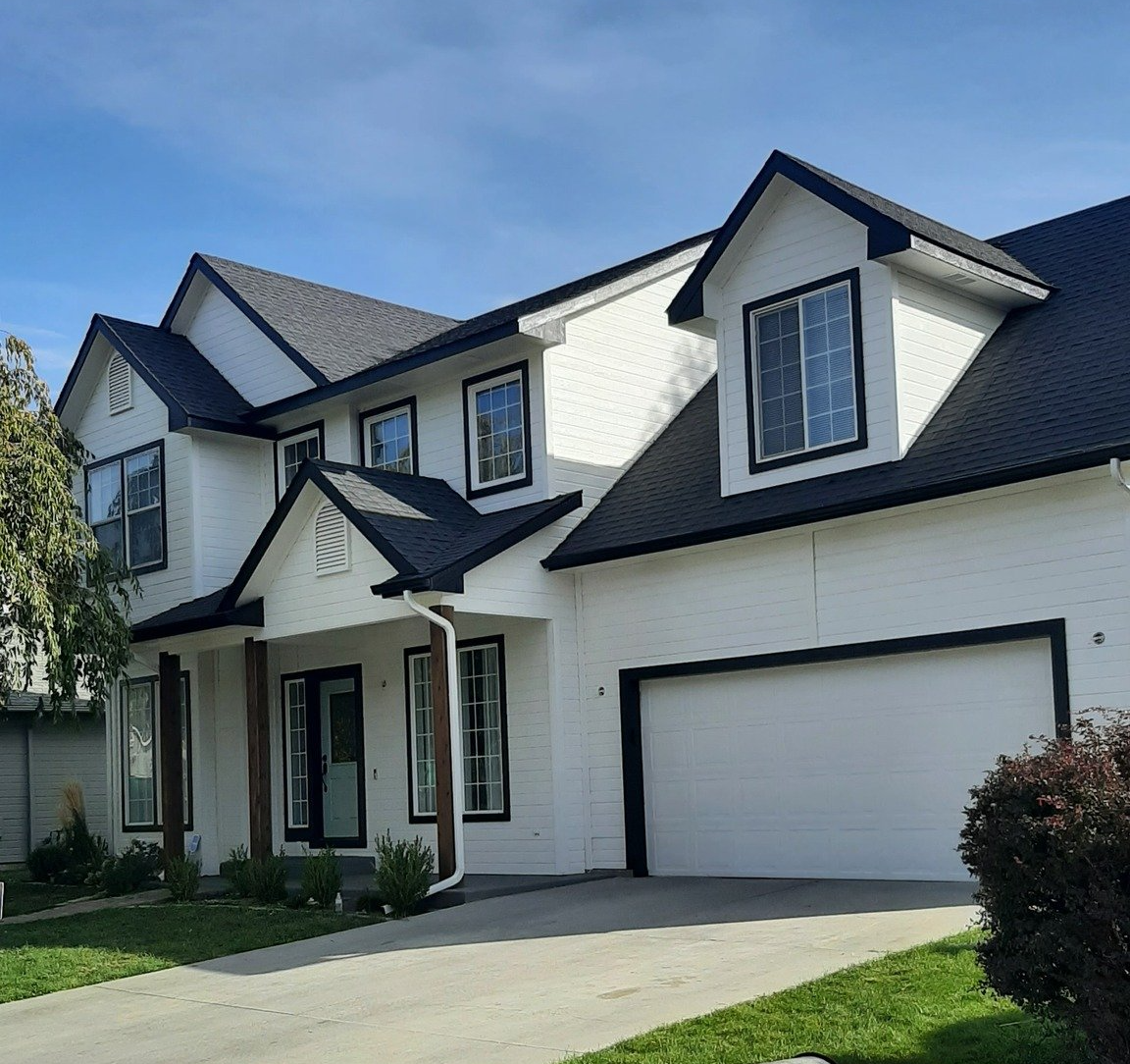 White two-story suburban house with black roof, double garage, and front lawn under a blue sky