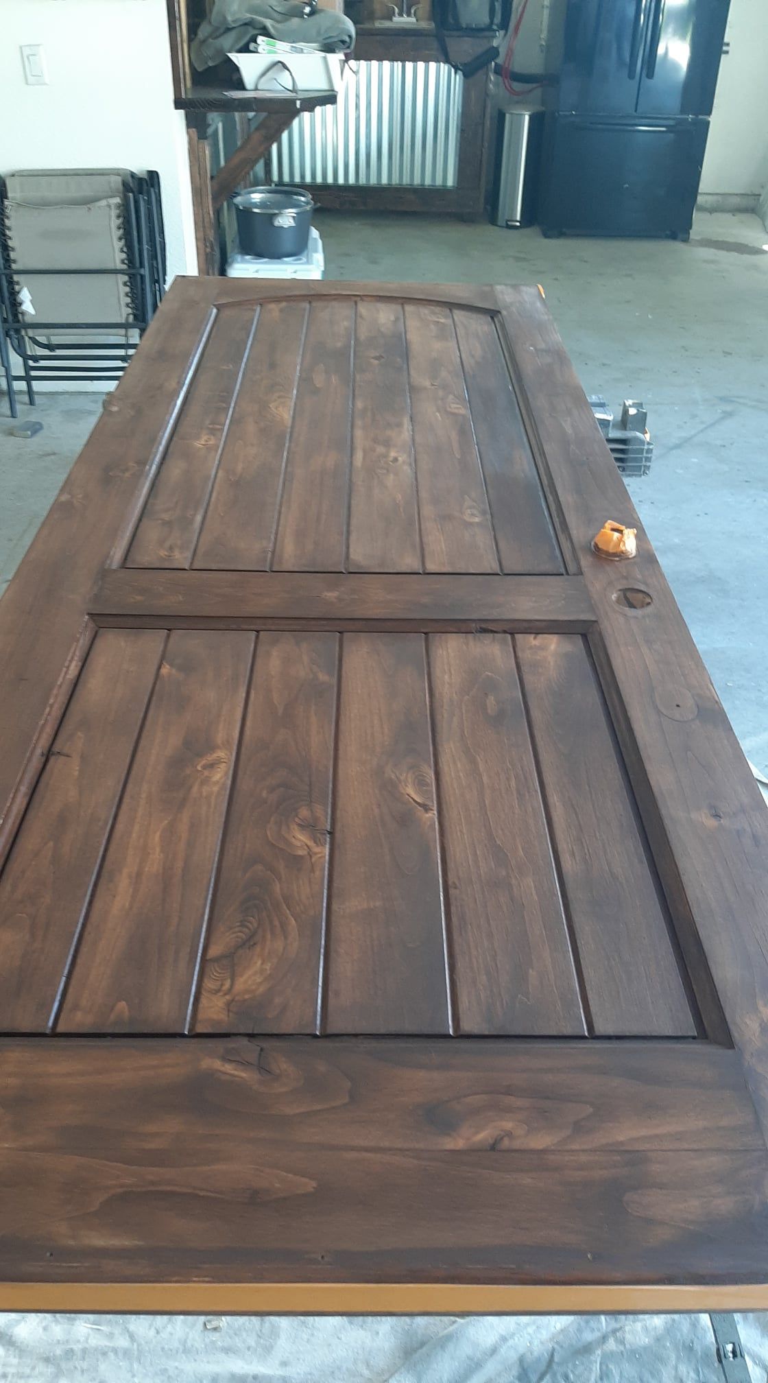 Wooden barn-style door lying flat indoors, with a dark wood finish and visible metal latch.