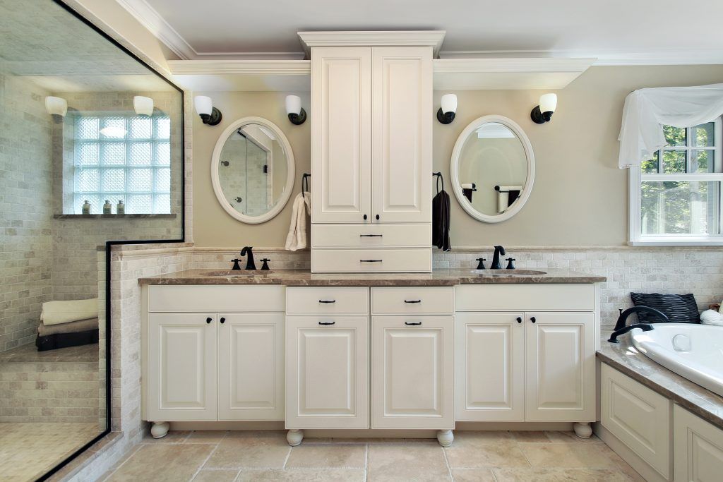 Elegant bathroom with double sinks, large mirrors, white cabinetry, and beige tile floors.