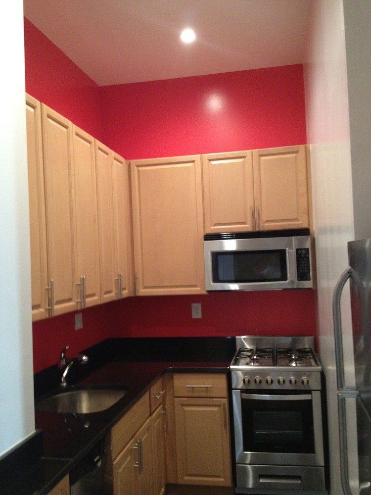 Compact kitchen with beige cabinets, red walls, black countertops, and stainless steel stove and microwave.