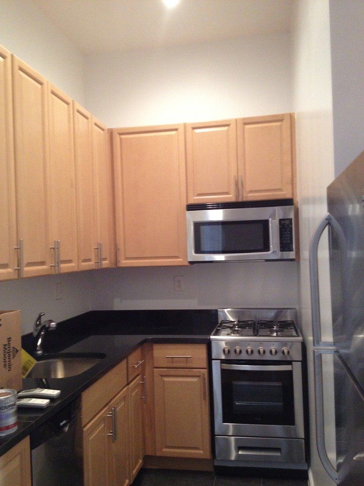 Small kitchen with light wood cabinets, black countertops, stainless stove, microwave, and refrigerator.