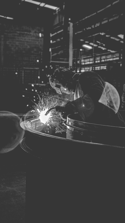 INDUSTRIE Een zwart-wit industriële scène met vonken die van las- of slijpmachines in een fabriek afspatten.
