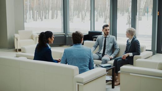 Vier mensen zitten in een lichte lounge en praten met elkaar rond een salontafel.