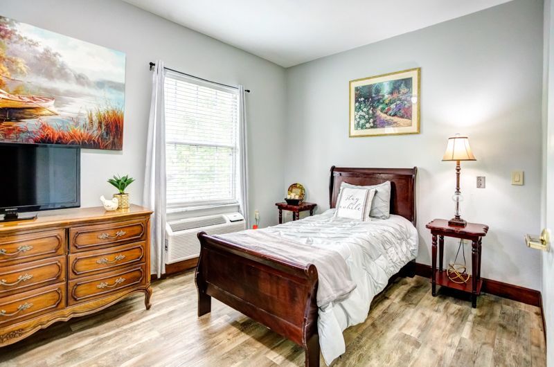 A bedroom with a single bed , dresser , nightstand and television.