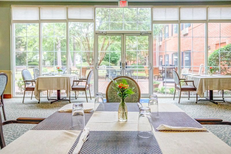 A dining room with tables and chairs and a vase of flowers on the table.