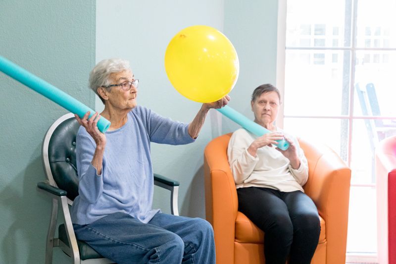 Two elderly women are sitting in chairs playing with balloons.