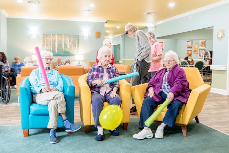 A group of elderly people are sitting in chairs in a living room playing with balloons.
