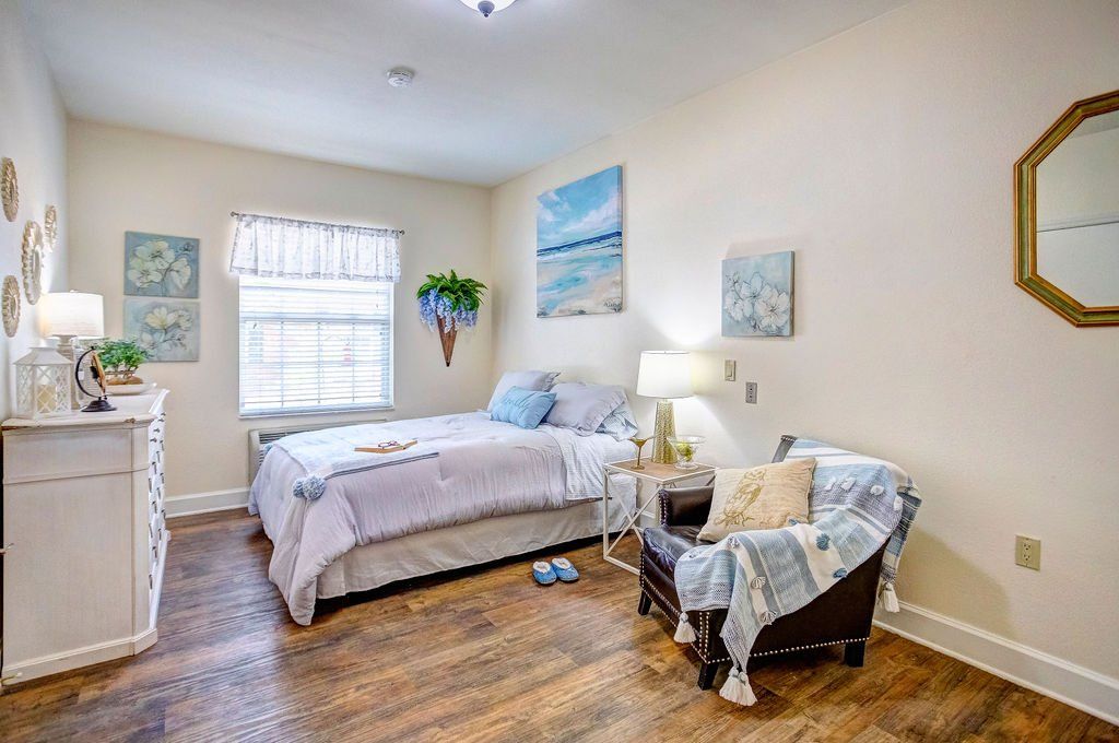 A bedroom with a bed , chair , dresser and mirror.