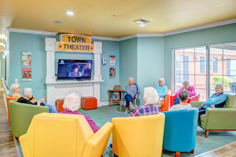 A group of elderly people are sitting in chairs in front of a television in a living room.