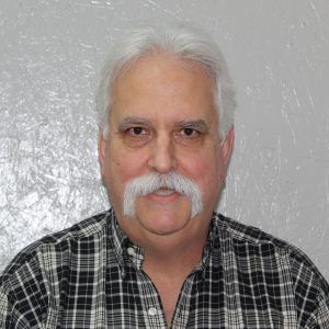 A man with a mustache is wearing a plaid shirt.