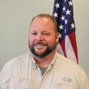 A man with a beard is smiling in front of an american flag.