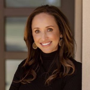 A woman wearing a black turtleneck and earrings is smiling for the camera.