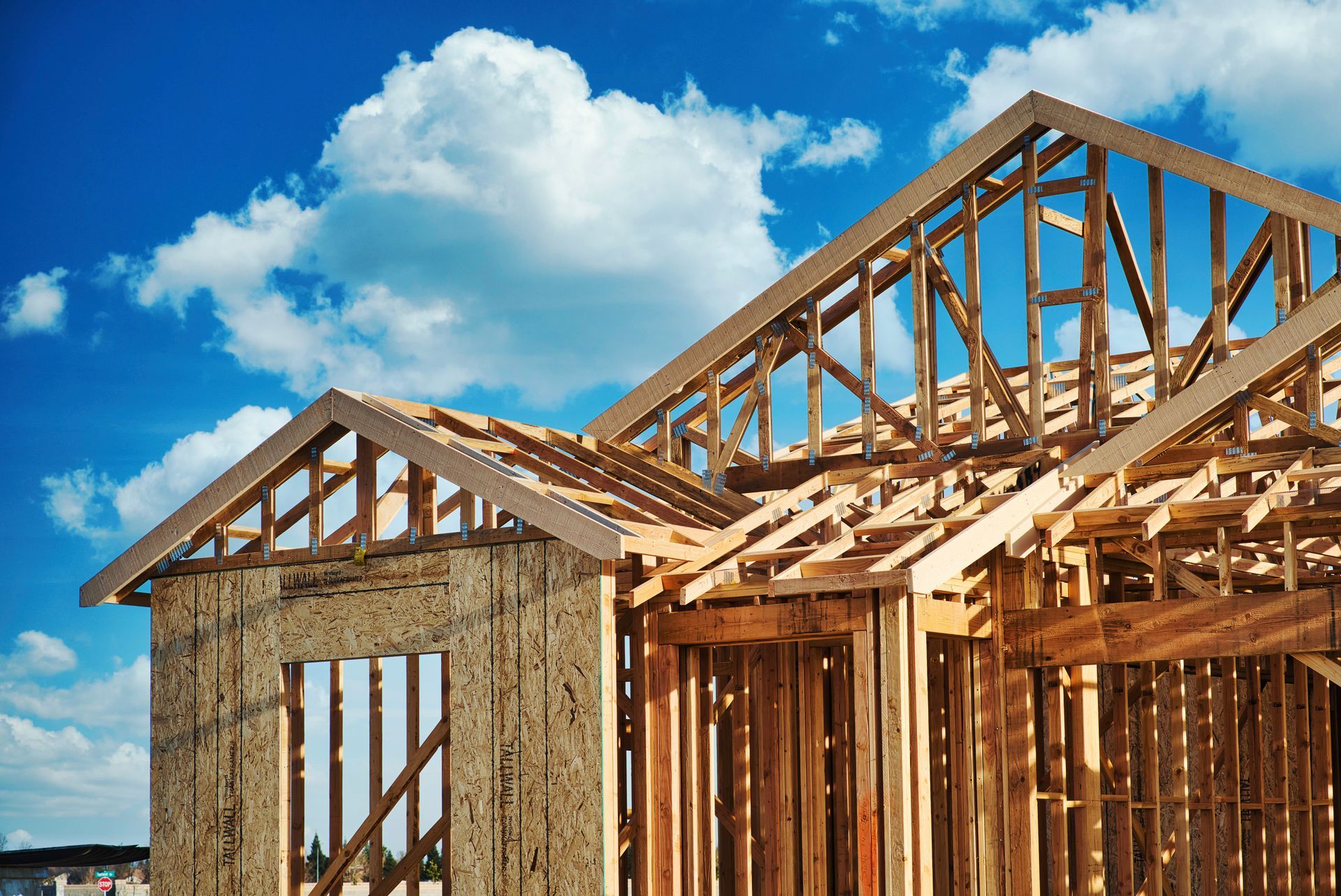Framed wooden house under construction against a blue sky with clouds.