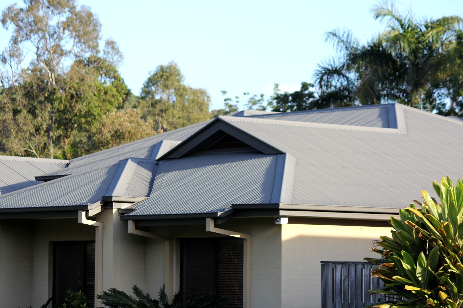Worker in orange safety gear using a drill to install metal roofing panels