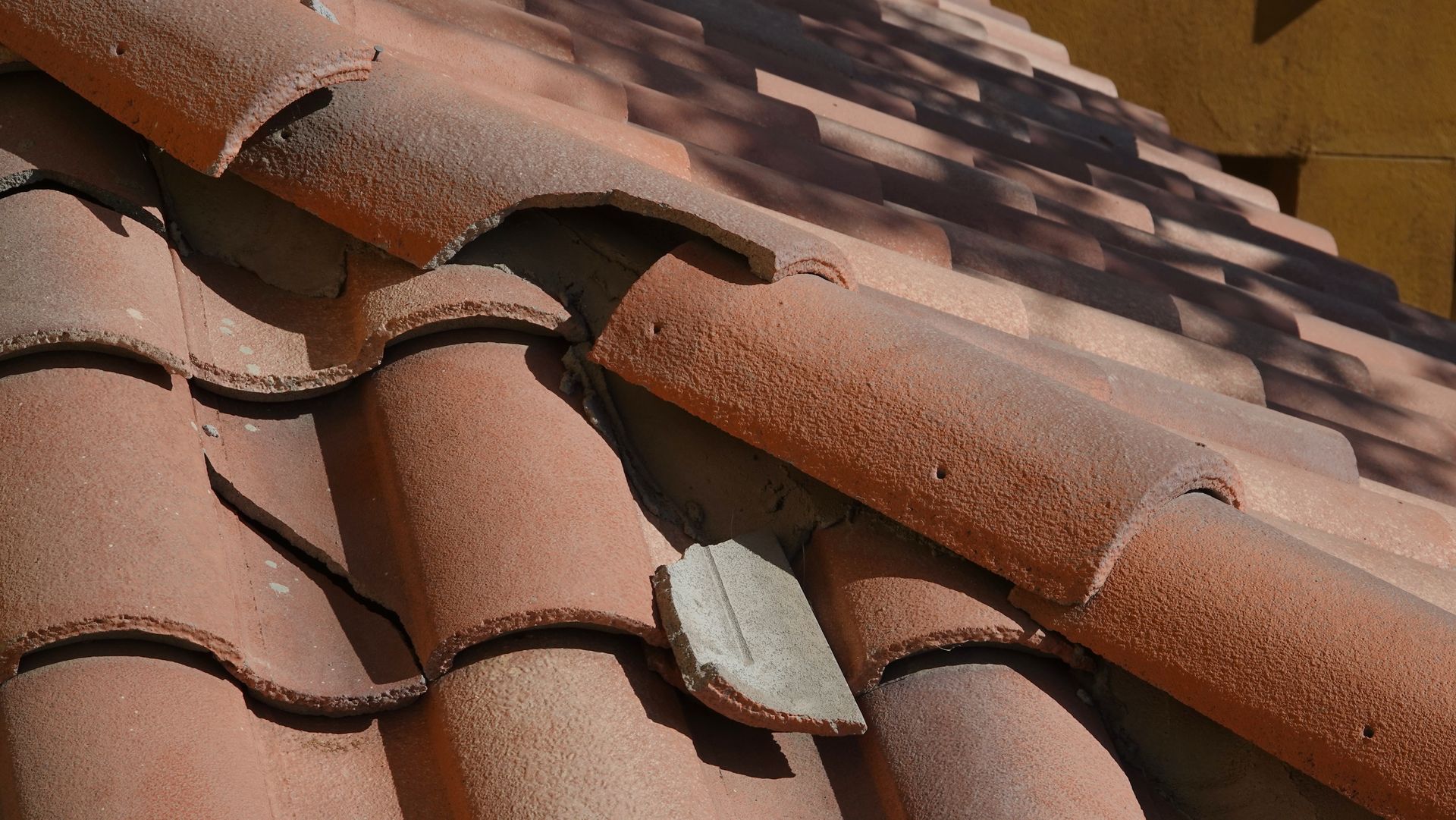 Close-up of reddish clay roof tiles with a few cracked and missing pieces on a tiled roof Close-up of reddish clay roof tiles with a few cracked and missing pieces on a tiled roof