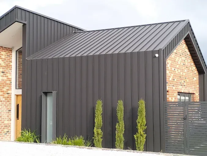 Modern house exterior with dark metal siding, brick accents, and a small front garden Modern house exterior with dark metal siding, brick accents, and a small front garden