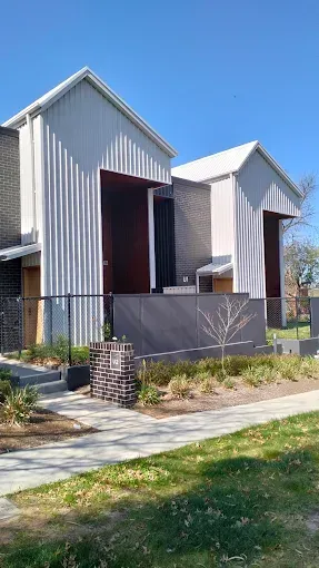 Modern gray houses with steep roofs and fenced front yards along a sidewalk under a blue sky Modern gray houses with steep roofs and fenced front yards along a sidewalk under a blue sky