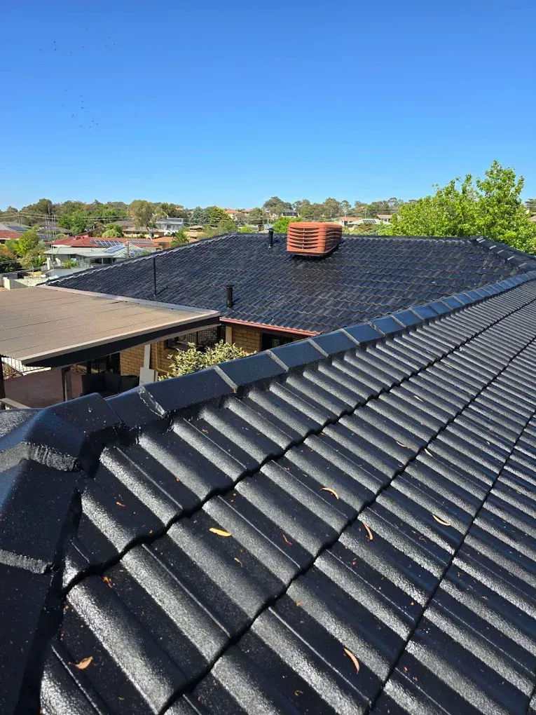 Partially installed terracotta roof tiles on a sloped roof under a clear blue sky
