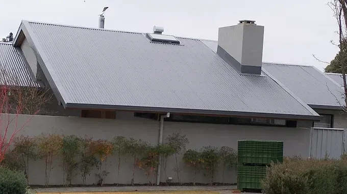 Gray house with a steep metal roof, a chimney, and a green gate behind a fence. Gray house with a steep metal roof, a chimney, and a green gate behind a fence.