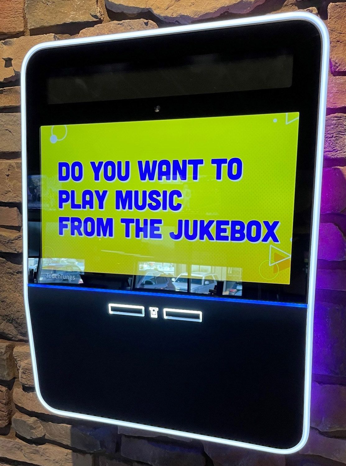 Jukebox kiosk on a brick wall, displaying 