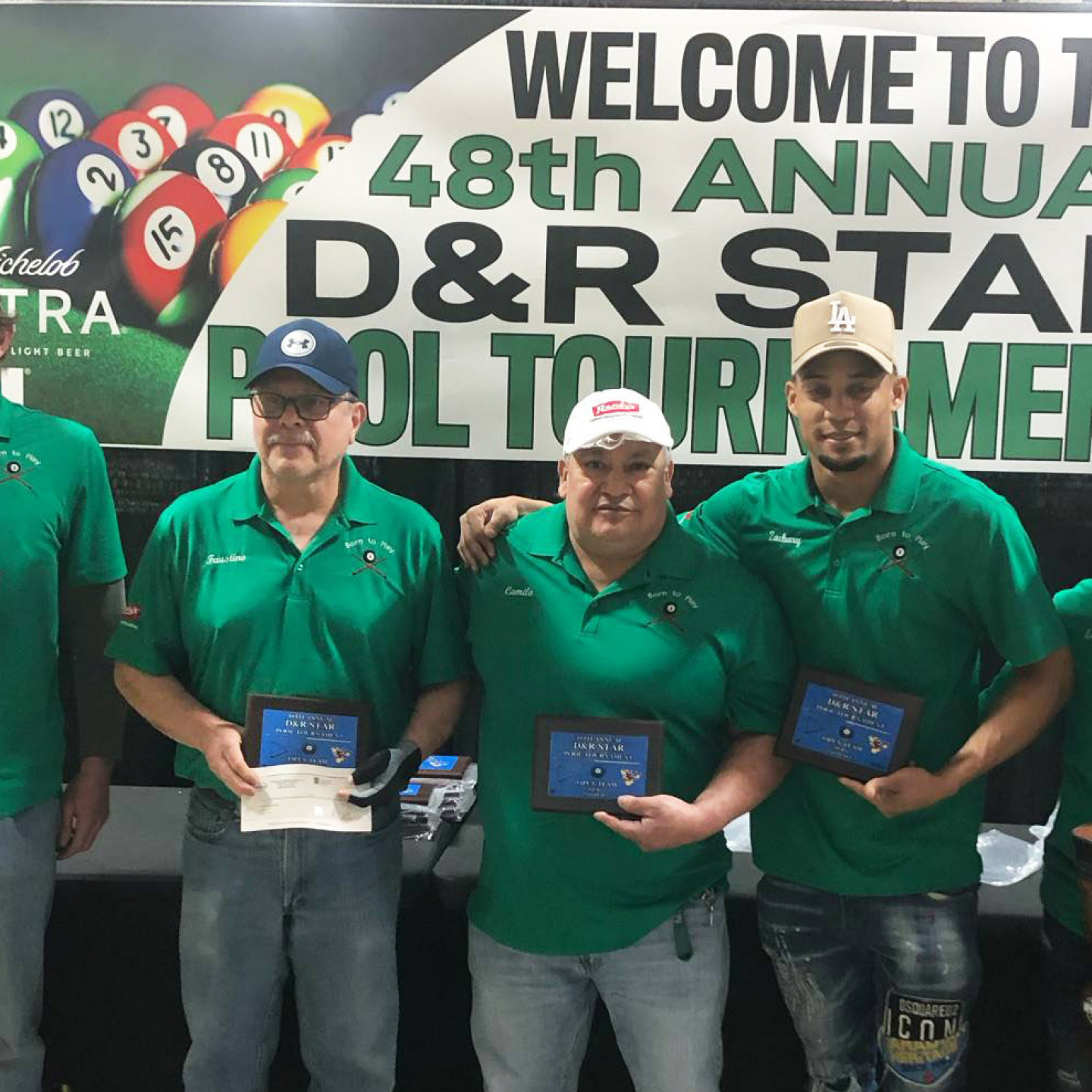 People holding trophies at the 48th Annual D&R Star Pool Tournament. They wear green shirts, standing in front of a banner.