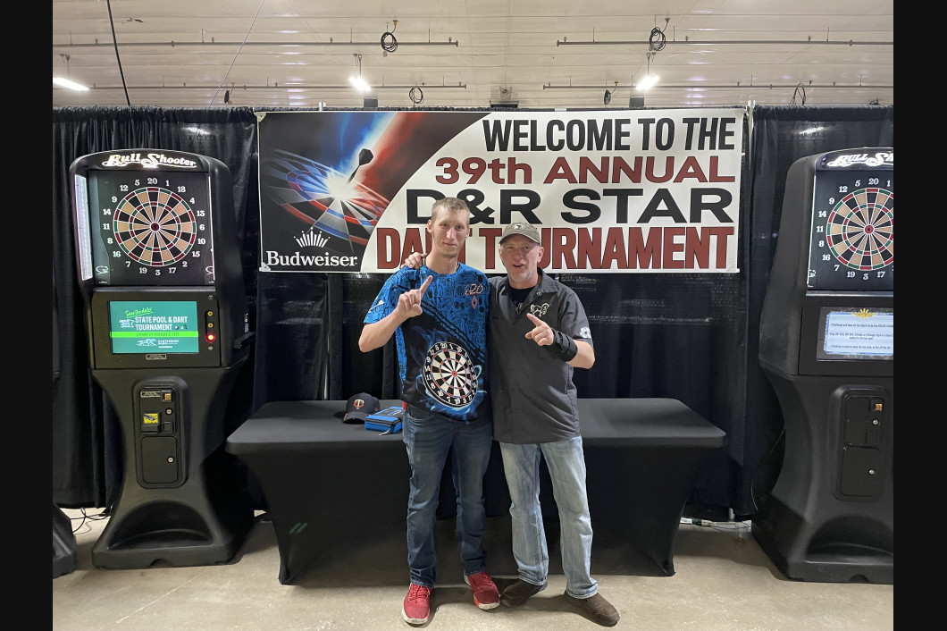 Two men pose with dart machines at the 39th annual D&R Star Dart Tournament.
