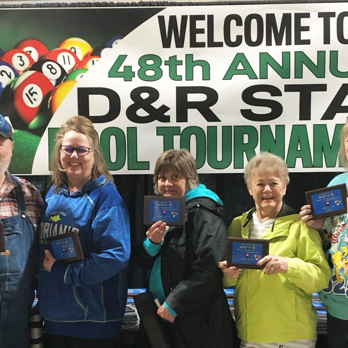People holding framed awards in front of a banner for a pool tournament.