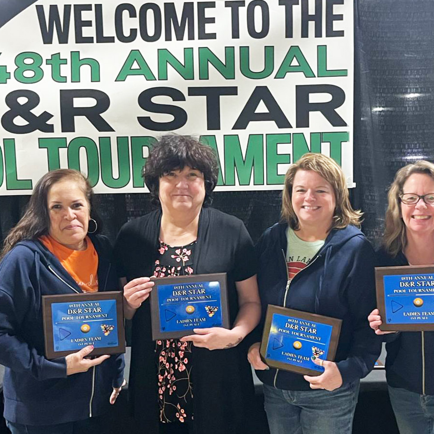 Four women holding award plaques stand in front of a banner that reads 