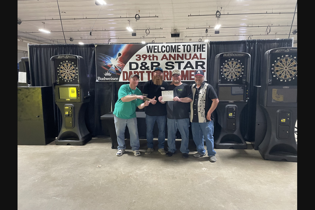 Men receiving award at the 39th Annual D&R Star Dart Tournament. They stand by dart machines on a stage.