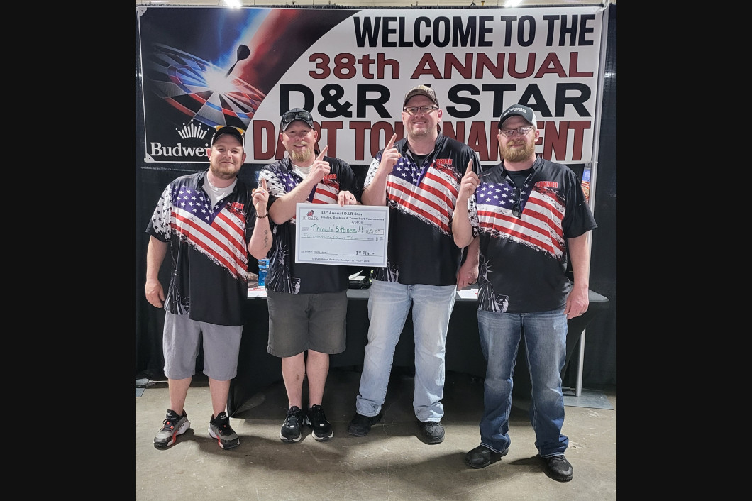 Four men holding a large check at the 36th Annual D&R Star Dart Tournament; American flag shirts.
