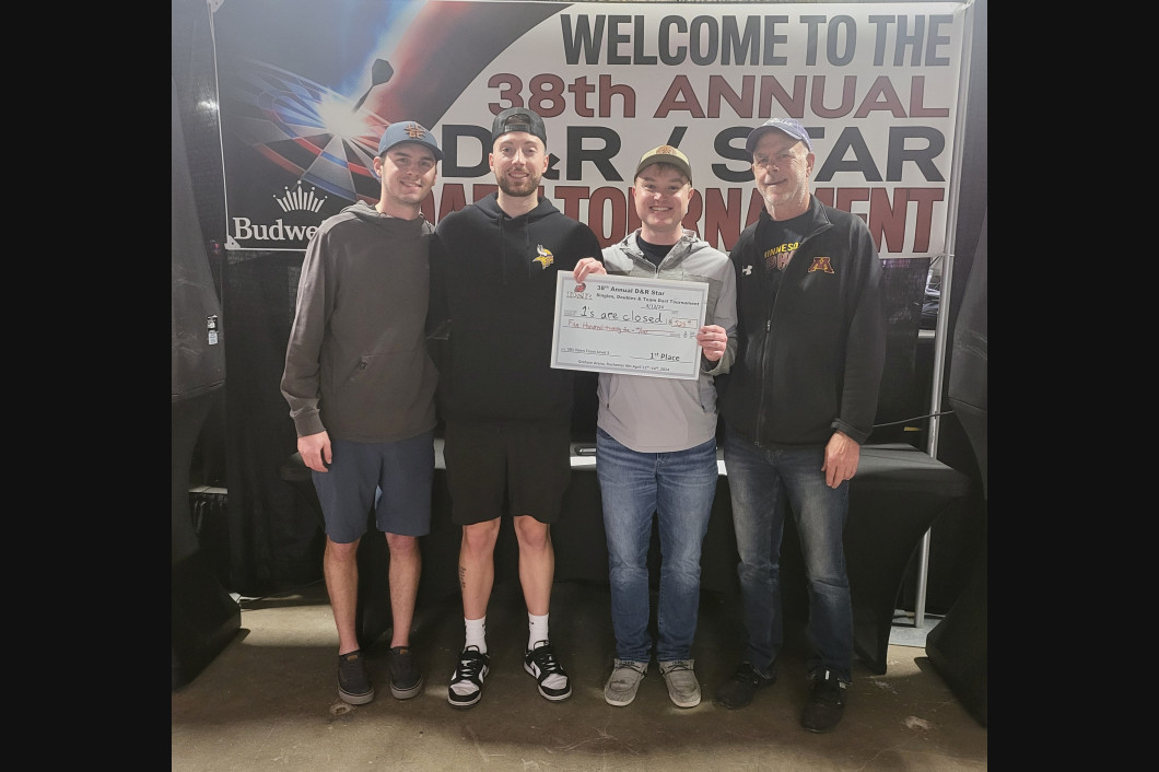 Four people standing in front of a banner. They hold a check. The banner reads 