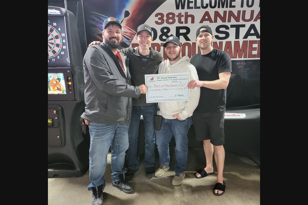 Four men holding a check at a tournament, a sign in the background reads 