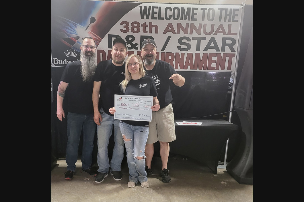 Group of four people posing in front of a banner for a D&B/Star tournament. They hold a sign.