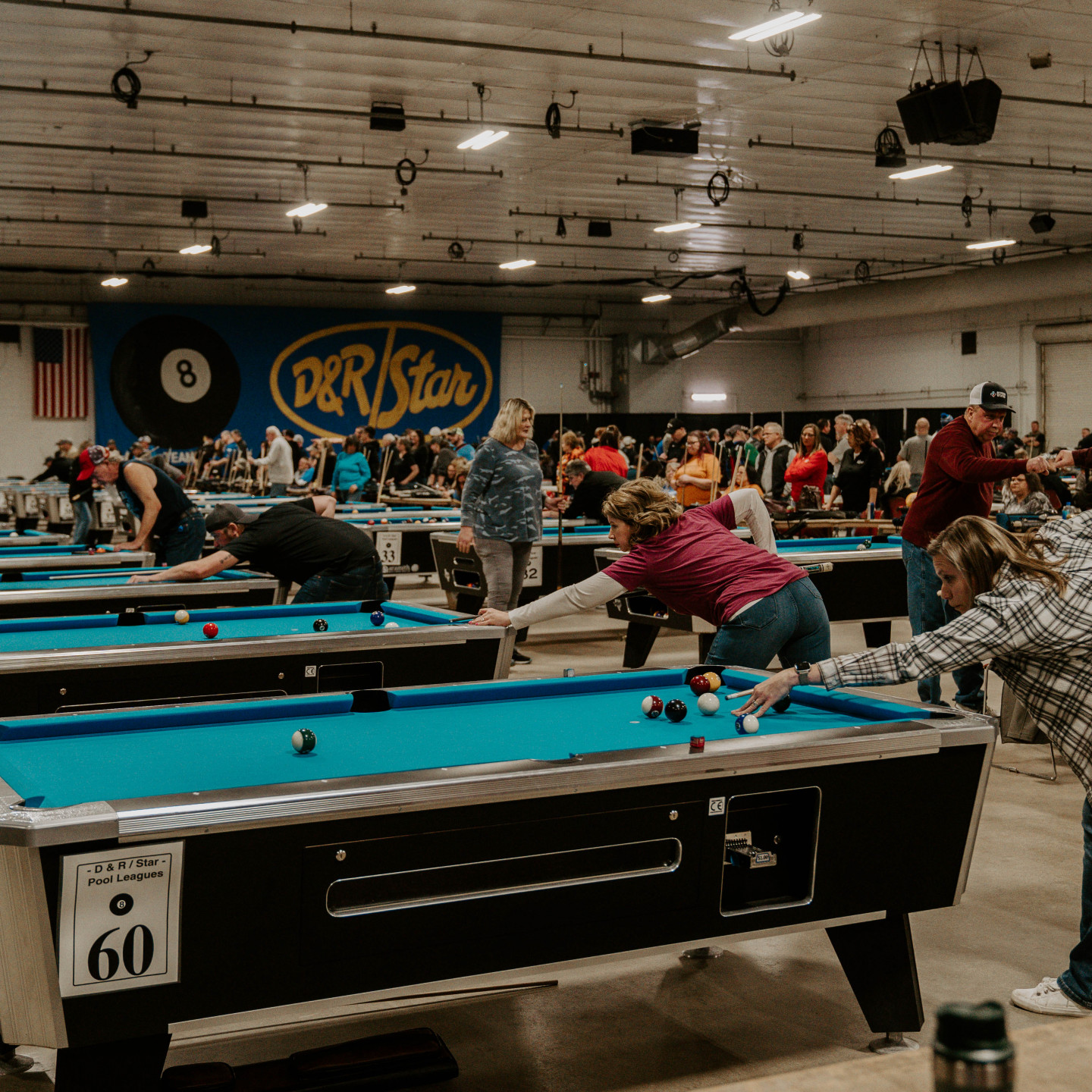 Pool tournament: People playing pool at multiple tables in a large indoor venue.