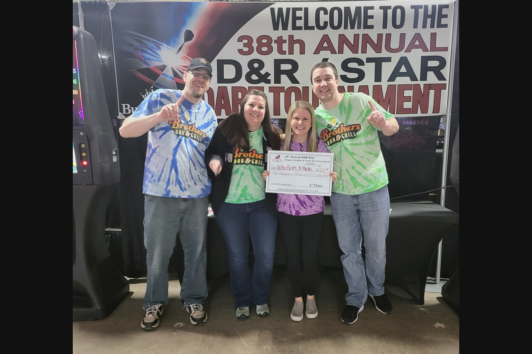 Four people pose with a prize check at the D&R Star Tournament. They wear tie-dye shirts, smiling in an event booth.