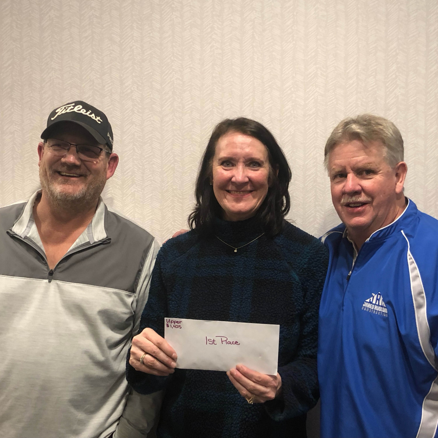 Three people smiling, woman holding envelope labeled 