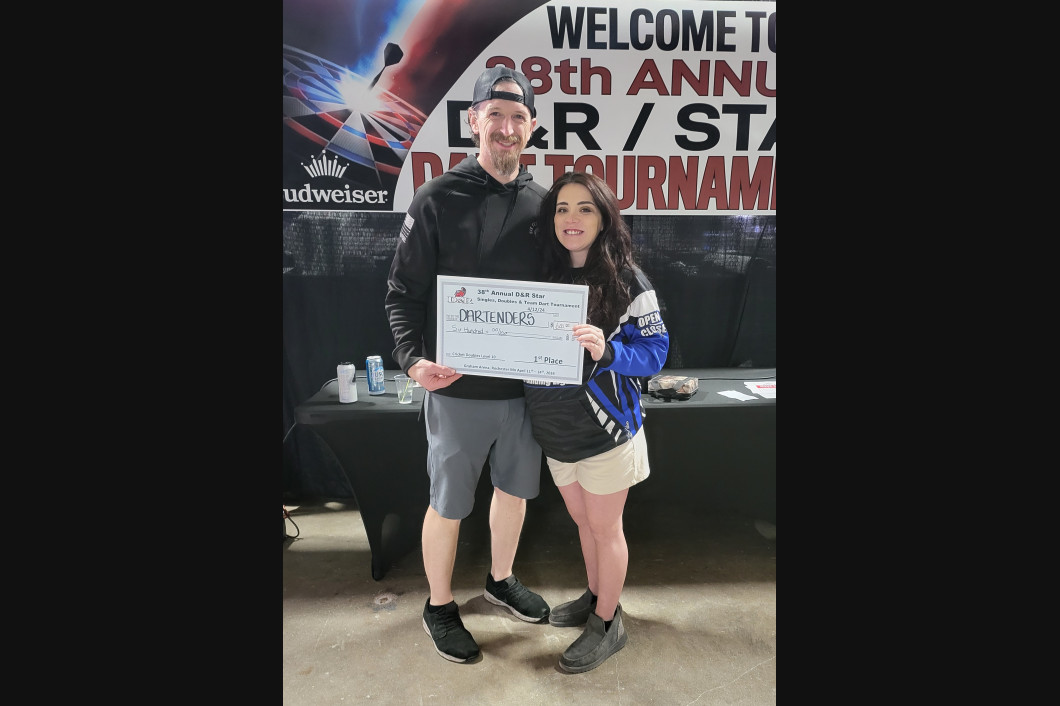 Two people hold a certificate at a tournament. A banner reads 